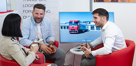 Two men and a woman sitting in front of a screen with a truck
